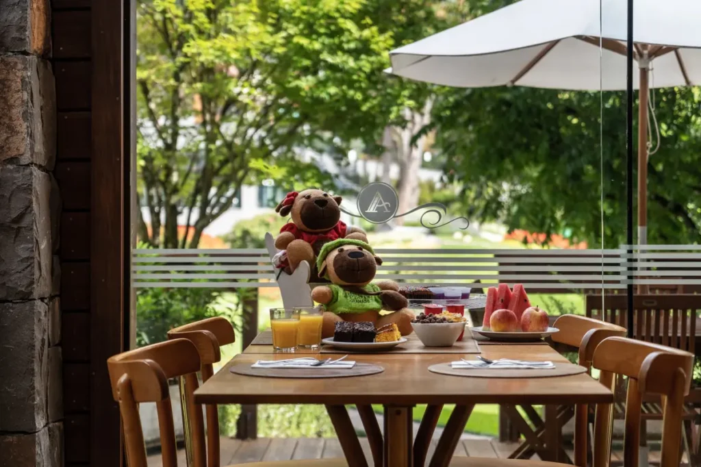 Café da manhã familiar com frutas, bolos e vista para os jardins do Hotel Alpestre Gramado.