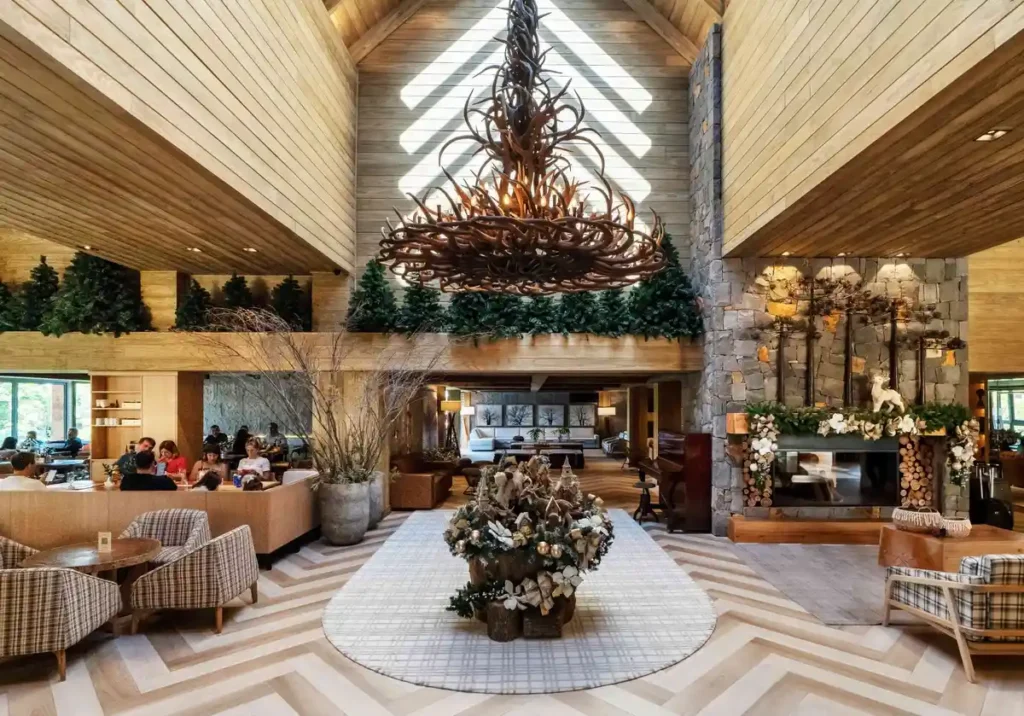 Lobby principal do Hotel Alpestre Gramado com lareira, lustre rústico e decoração sofisticada.