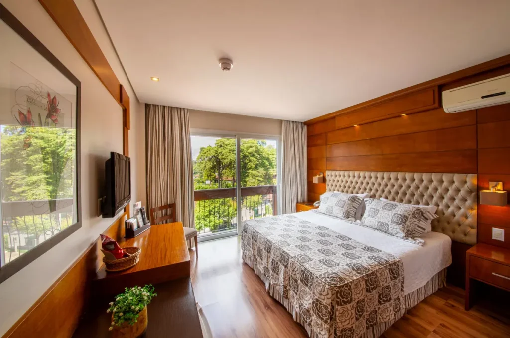 Quarto Super Luxo Vista Cidade do Hotel Alpestre com cama de casal e decoração elegante.