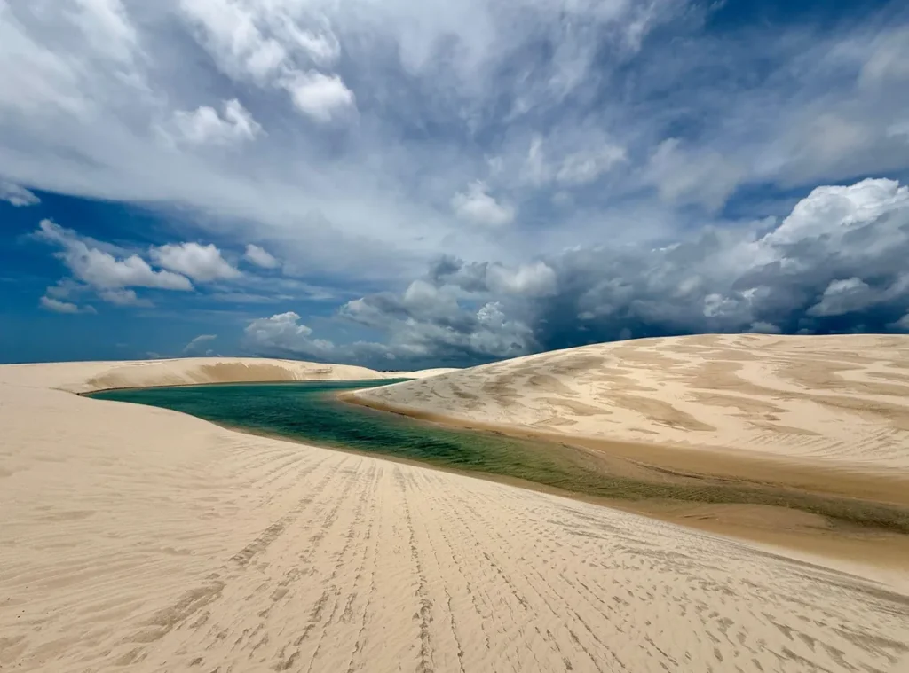 Lagoa cercada por dunas dos Lençóis Maranhenses sob céu dramático com nuvens carregadas.