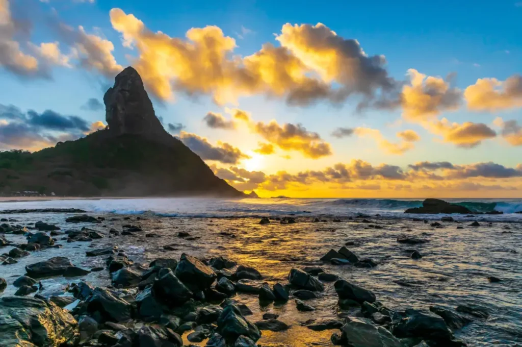 Pôr do sol com Morro do Pico e praia rochosa em Fernando de Noronha.