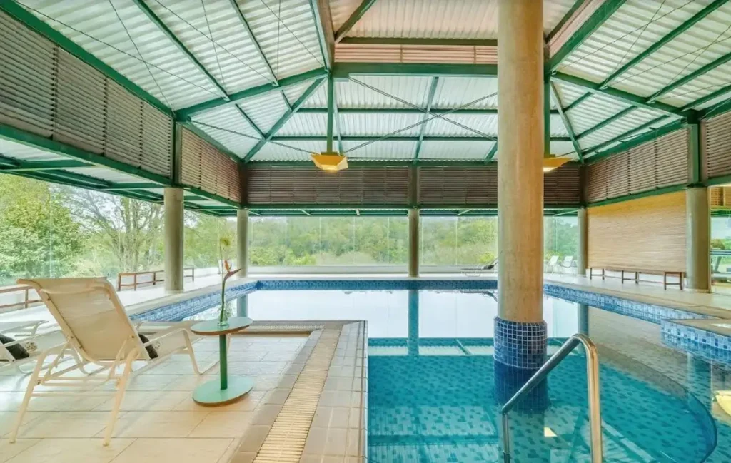 Piscina coberta do Almenat Embu das Artes, com espreguiçadeiras e vista para a natureza.
