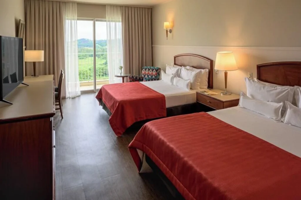Quarto do Bourbon Resort Atibaia com duas camas, varanda e vista para a área verde.