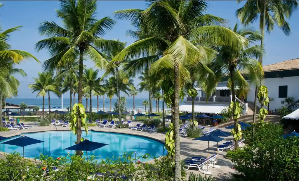 Área da piscina do Casa Grande Hotel Resort & Spa cercada por coqueiros e próxima à praia.