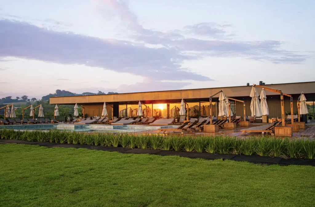 Área de lazer do Clara Ibiúna Resort com piscina, espreguiçadeiras, paisagismo e vista ao pôr do sol.