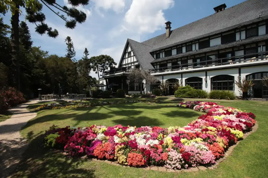 Fachada do Grande Hotel Campos do Jordão cercada por jardins floridos e natureza.