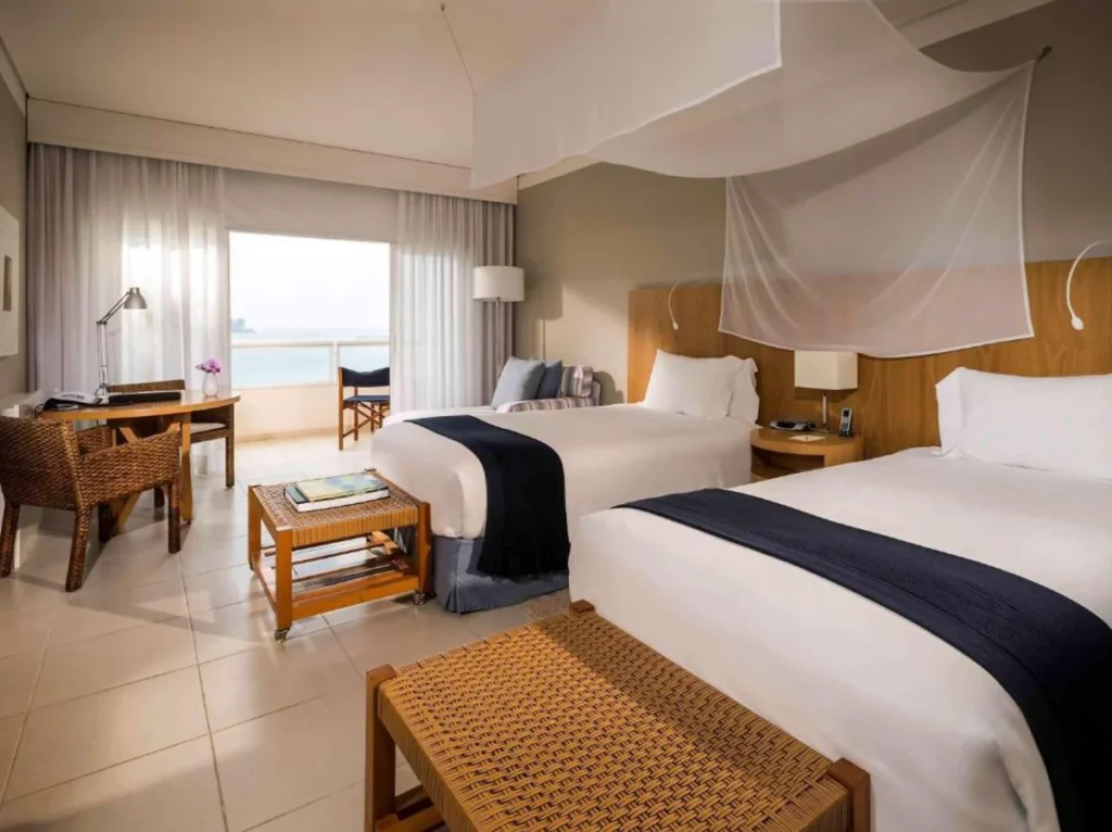 Acomodação do Hotel Jequitimar com duas camas, varanda e vista para o mar.