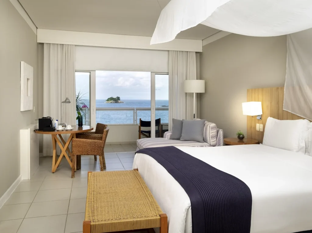 Quarto do Hotel Jequitimar com cama de casal, varanda e vista privilegiada para o mar.