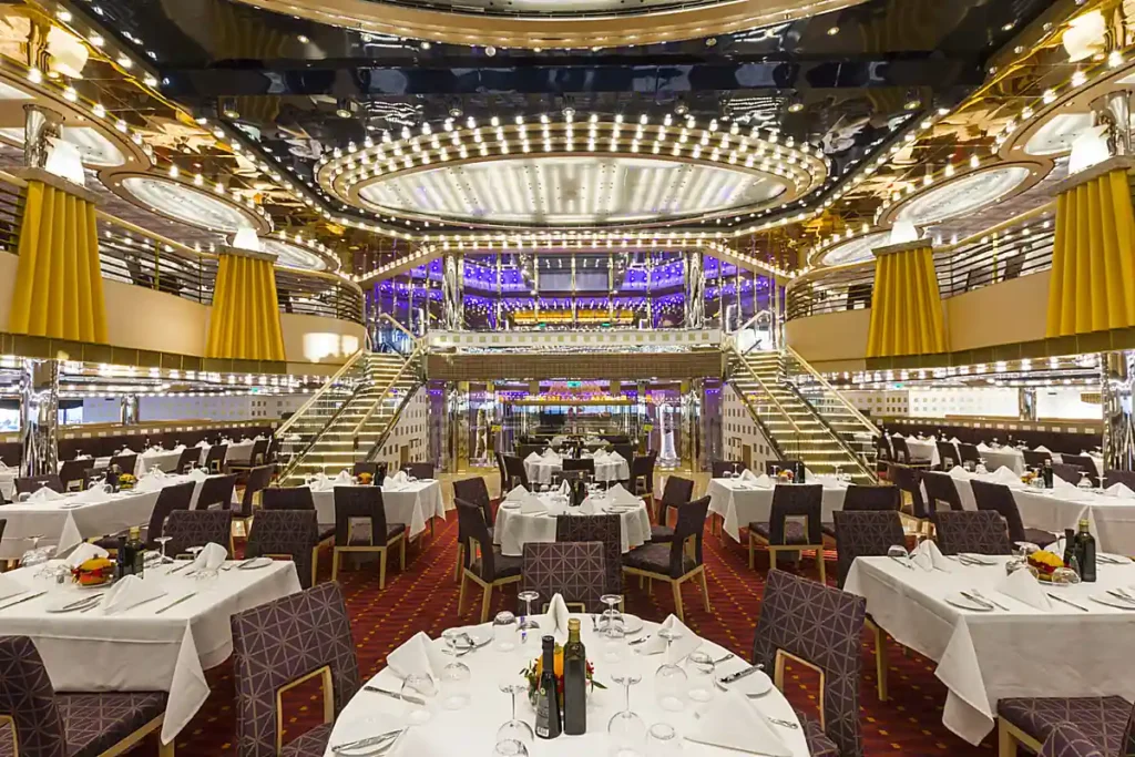 Ambiente interno de restaurante de cruzeiro, com salão de jantar, mesas preparadas e iluminação decorativa.