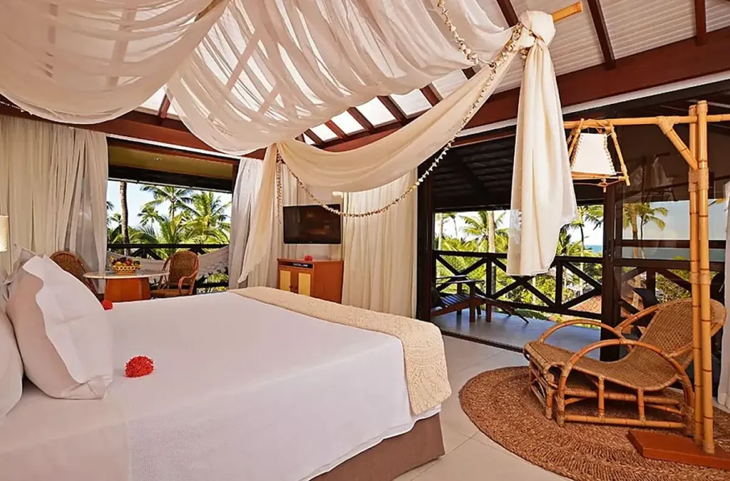 Acomodação do Nannai Muro Alto com decoração tropical, cama com tecidos leves e varanda integrada à natureza.