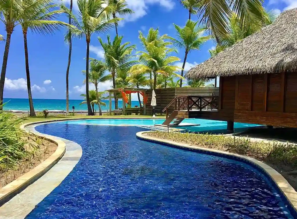 Piscina entre coqueiros e bangalôs do Nannai Muro Alto, com vista para o mar no litoral de Pernambuco.